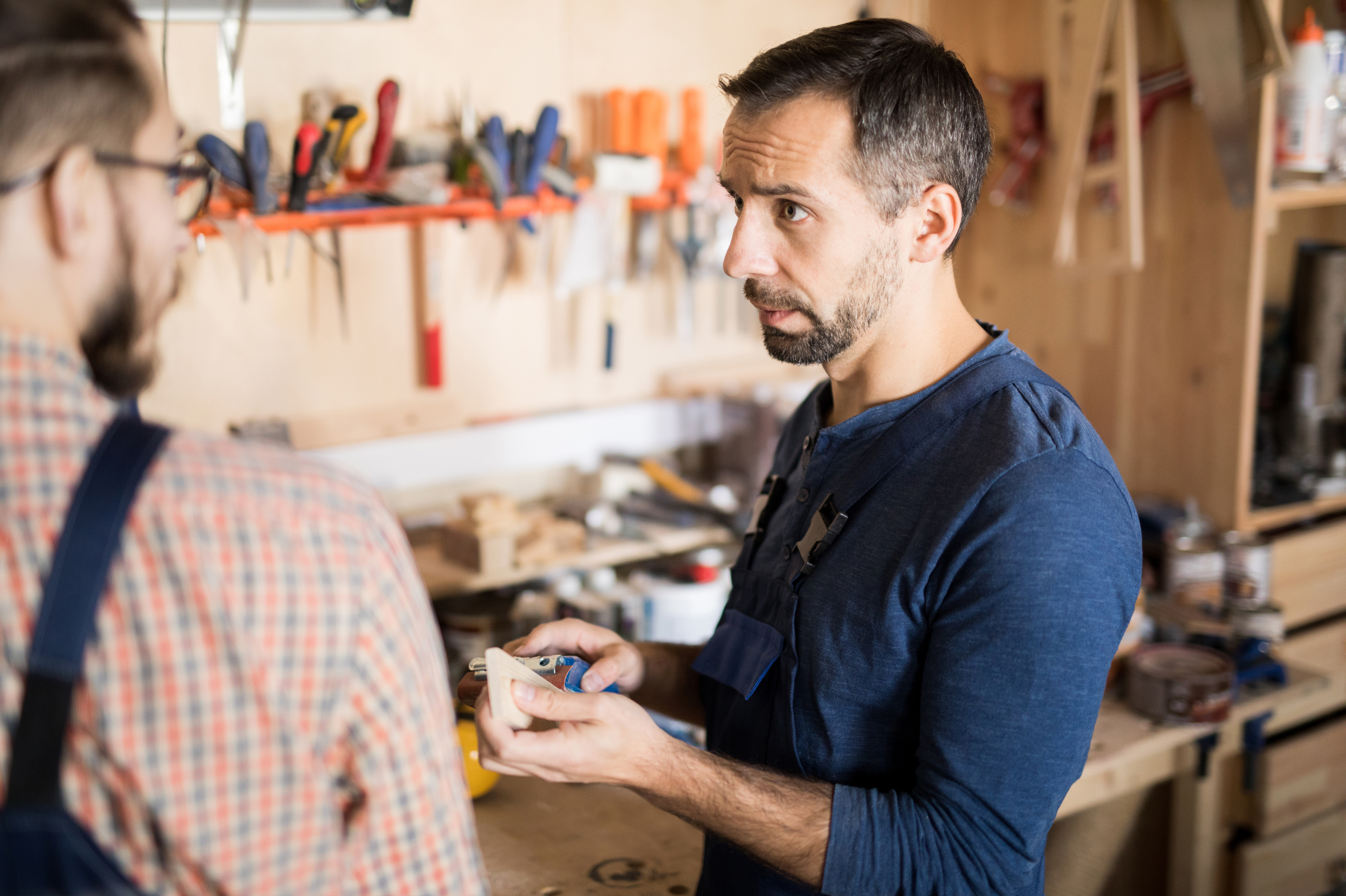 Portrait of mature bearded carpenter talking to apprentice teaching him woodworking craft, copy space