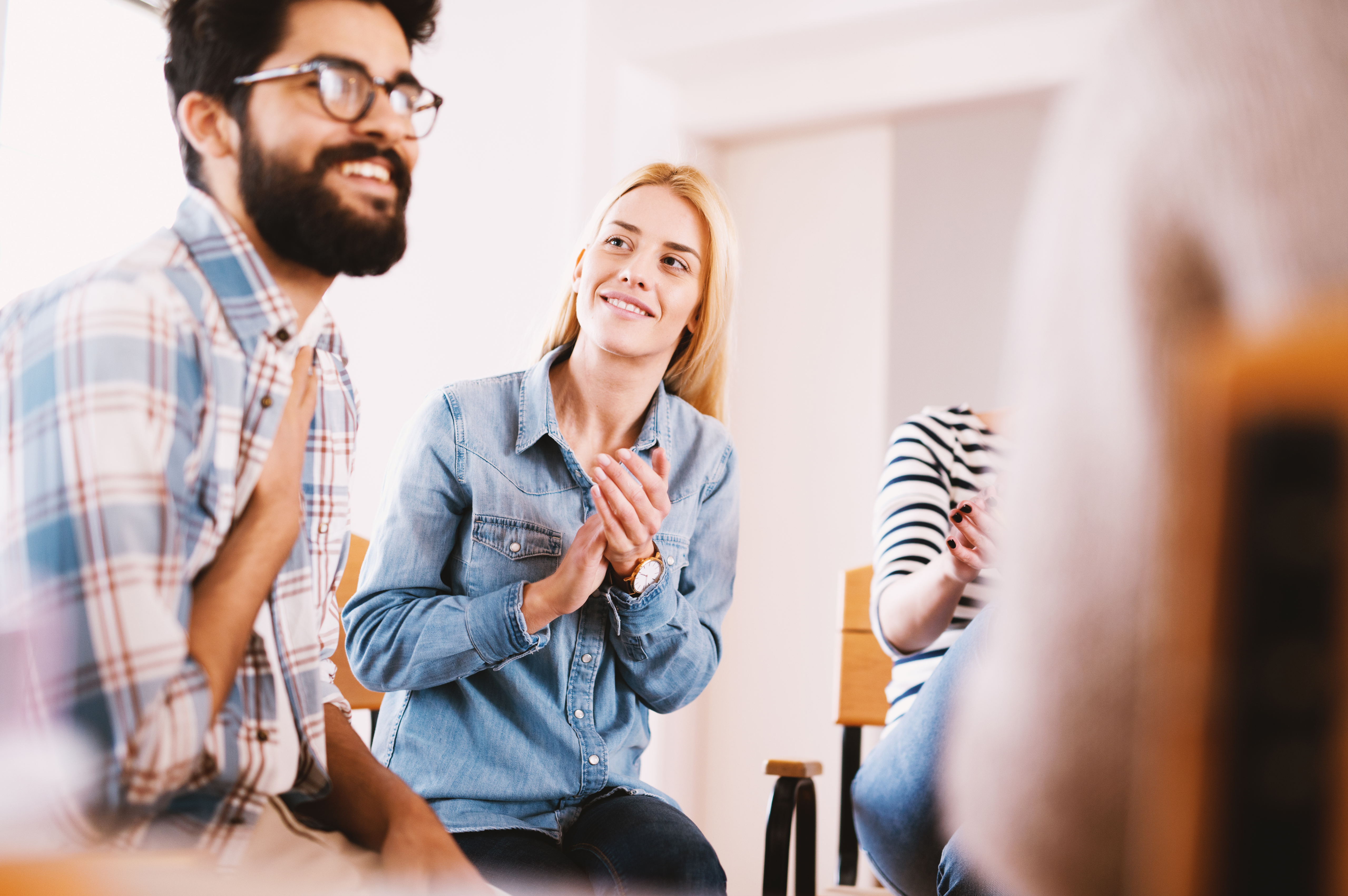 Young addicted people having celebrating situation while sitting together on special group therapy. Handsome hipster guy smiling after his confession and progress.