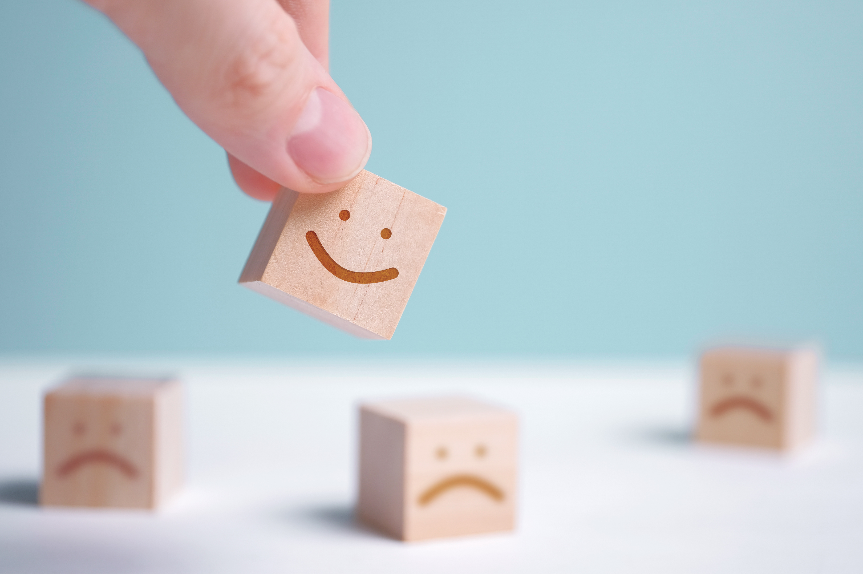 A man holds a wooden cube with a picture of a positive face on the background of negative emotions. Close up.